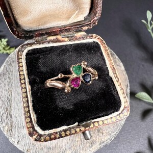 May include: A gold ring with three heart-shaped gemstones. The gemstones are green, pink, and blue.