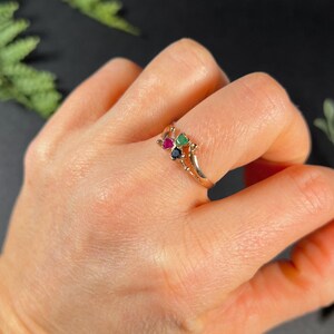 May include: A gold ring with three small gemstones: a green emerald, a red ruby, and a black sapphire.