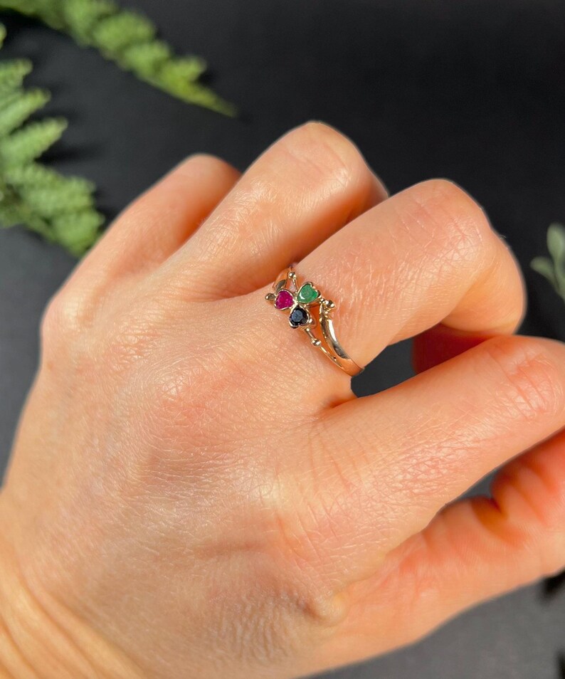 May include: A gold ring with three small gemstones: a green emerald, a red ruby, and a black sapphire.