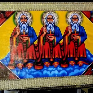 May include: A framed painting depicting three figures with white beards and halos, wearing red and blue robes, seated on a cloud. The background is yellow with a gold frame.