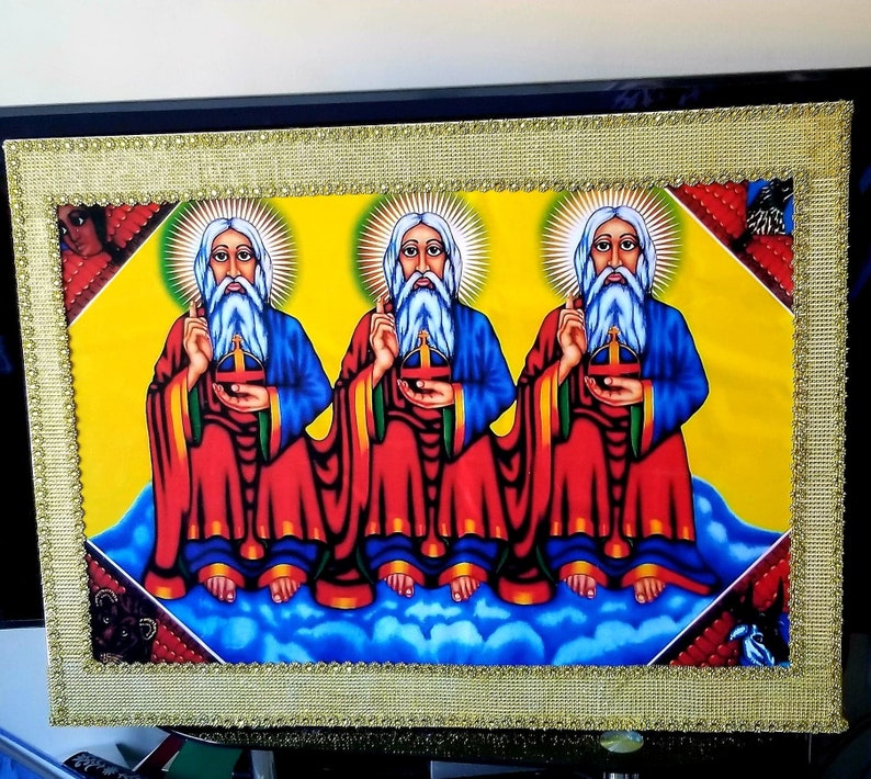May include: A framed religious artwork featuring three figures with long white beards and halos, wearing red and blue robes, seated on clouds against a yellow background.