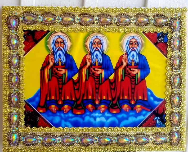 May include: A framed religious icon depicting three figures with long white beards and halos. They are wearing red and blue robes and holding a cross. The frame is decorated with gold and iridescent beads.