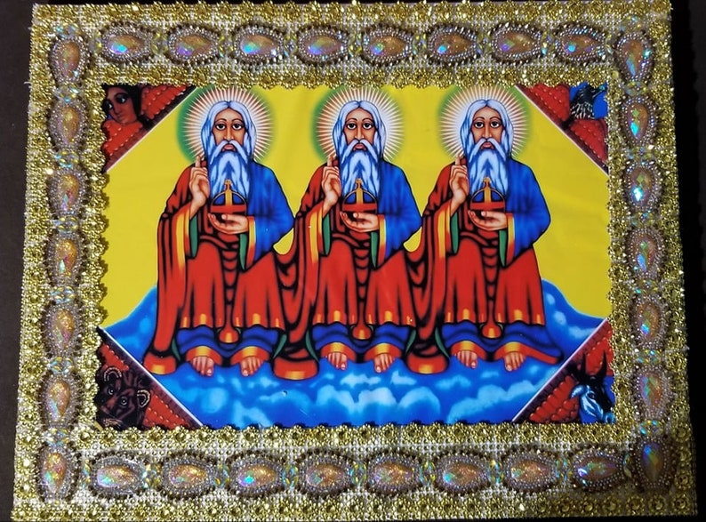 May include: A framed religious icon depicting three figures with white beards and halos, wearing red and blue robes, holding a cross and sitting on clouds against a yellow background.