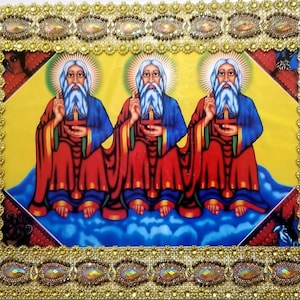 May include: A framed religious icon depicting three figures with long white beards and red robes. The figures are holding crosses and are surrounded by a gold frame with ornate details.