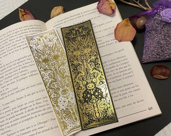 May include: Two gold bookmark designs with intricate patterns and illustrations. One bookmark is on a white background and the other is on a black background. Both bookmarks feature a sword, eyes, and other mystical symbols.