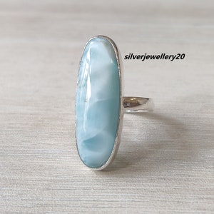 May include: A silver ring with a light blue oval-shaped gemstone. The gemstone has a swirling pattern and a smooth, polished finish.