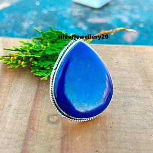 Könnte beinhalten: Ein silberner Ring mit einem großen, tropfenförmigen Lapislazuli-Stein. Der Stein ist tiefblau mit weißen Adern, die durch ihn verlaufen.