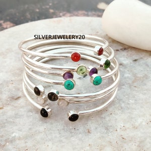 Pode incluir: Uma pilha de pulseiras de prata com pedras preciosas de diferentes cores. As pedras preciosas incluem vermelho, verde, roxo, turquesa, preto e branco.