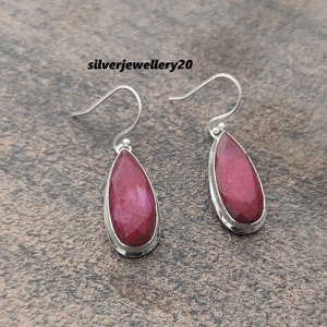 Peut inclure: Paire de boucles d'oreilles pendantes en argent avec des pierres précieuses en rubis taillées en forme de goutte d'eau. Les boucles d'oreilles ont un design simple avec une fermeture à crochet. Les pierres sont d'un rouge profond.