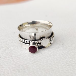 Peut inclure: Une bague tournante en argent avec une pierre précieuse rouge et un charme en forme de cœur. La bague est en argent sterling et a une bande perlée.