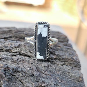 May include: A silver ring with a rectangular black and white stone. The stone is set in a silver frame with a twisted rope design. The ring has a split shank design.