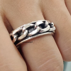 Peut inclure: Une bague en argent avec un motif de chaîne. La bague est épaisse et a une large bande.