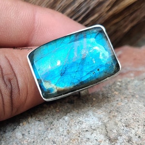 May include: A silver ring with a large, rectangular, iridescent blue labradorite gemstone. The stone has a unique, natural pattern of veins and inclusions.