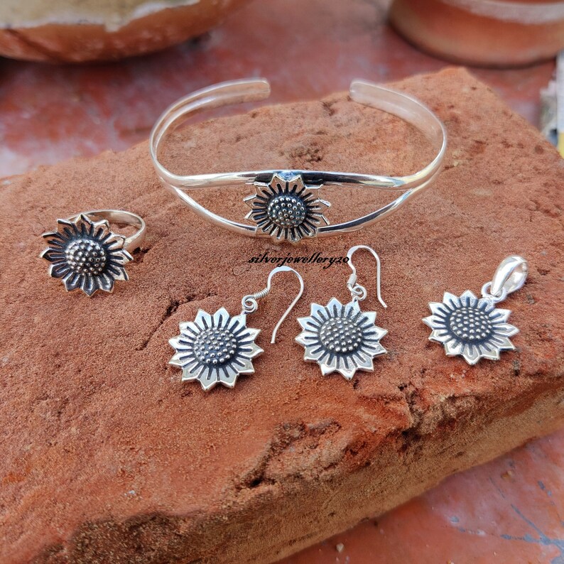 May include: A silver sunflower jewelry set with a bangle, ring, earrings, and pendant. The jewelry is made of sterling silver and features a detailed sunflower design.