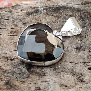Pode incluir: Um pingente de prata em forma de cora&ccedil;&atilde;o com uma pedra preciosa de quartzo fumado escuro. O pingente tem uma argola para prender a uma corrente.