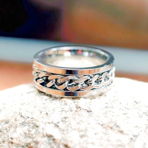 May include: A silver ring with a chain-link design. The ring is made of metal and has a smooth finish.