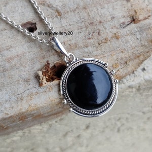 Peut inclure: Un collier en argent avec un pendentif en onyx noir. Le pendentif est rond et a une bordure en argent avec un motif de corde. Le pendentif est serti dans une bélière en argent.