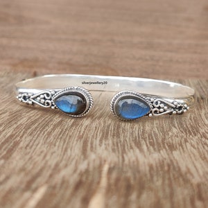Puede incluir: Pulsera de brazalete de plata con dos piedras de labradorita en forma de lágrima. La pulsera tiene un diseño delicado y adornado con pequeñas cuentas y espirales.