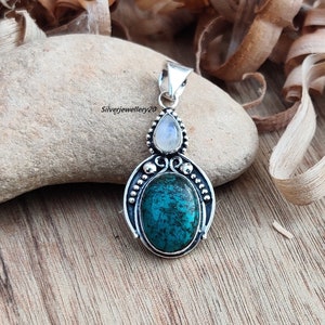 May include: Silver pendant featuring a turquoise gemstone surrounded by a silver filigree design. A smaller moonstone gemstone is set above the turquoise.