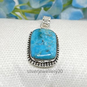 May include: A rectangular turquoise pendant with a silver-colored bezel and bail. The turquoise stone has a mottled blue-green appearance. The bezel is decorated with small, round beads. The text "silverjewellery20" is at the bottom.