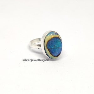 May include: A silver ring with a blue and yellow oval gemstone. The gemstone has a sparkly, iridescent finish.