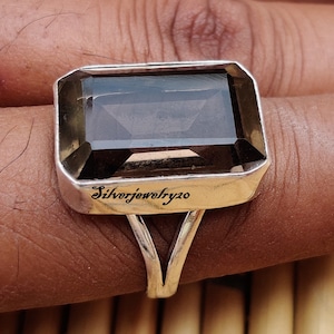 May include: A silver ring featuring a large, rectangular, smoky quartz gemstone. The ring has a simple, elegant design with a split band. The inscription "Silverjewelry20" is engraved on the band.