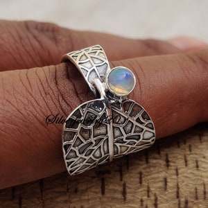 May include: A silver ring with a delicate leaf design and a round opal gemstone. The ring is open and adjustable.