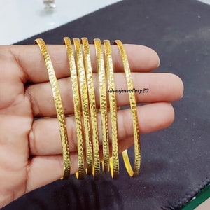 Pode incluir: Um conjunto de dez pulseiras de metal martelado de cor dourada. As pulseiras estão empilhadas e têm aproximadamente 1,25 cm de largura.
