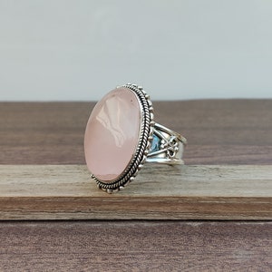 May include: A silver ring with a large oval-shaped pink rose quartz gemstone. The ring has intricate silver detailing around the stone and on the band.