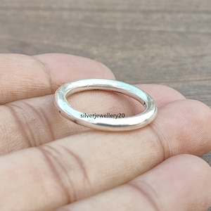 May include: A simple silver ring with a smooth, rounded surface. The ring is shown on a hand, but the ring itself is the focus of the image.
