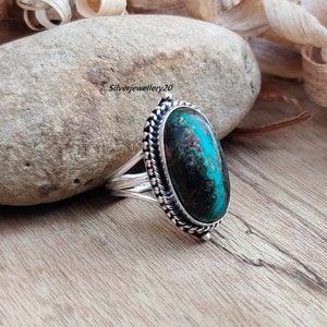 May include: A silver ring with a large oval turquoise gemstone. The ring has a detailed silver band with a braided design.
