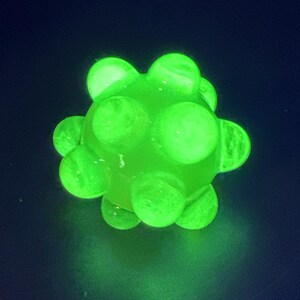May include: A glowing green, spherical object with multiple rounded protrusions. The object is illuminated against a dark background, creating a vibrant, eye-catching effect. The overall shape resembles a spiky ball.