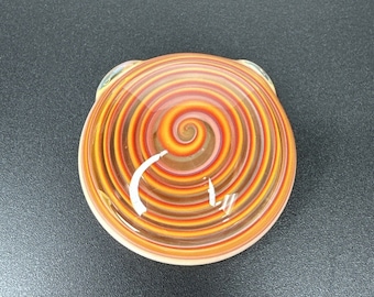 May include: A round glass piece with a swirling pattern of orange, red, and white. The piece has a smooth, glossy finish.