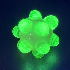 May include: A glowing green, spiky ball against a dark blue background. The ball has a central sphere with rounded protrusions, all emitting a bright, neon green light. The overall shape resembles a stylized virus or a playful, glowing toy.