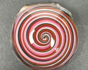 Könnte beinhalten: Ein runder Glas-Briefbeschwerer mit einem wirbelnden Muster in Rosa, Weiß, Rot und Blau.