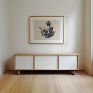 Pu&ograve; includere: Un mobile in legno chiaro con tre ante bianche. Il mobile &egrave; posto su un pavimento in legno chiaro. Un disegno in bianco e nero incorniciato di una persona seduta e che legge un libro &egrave; appeso al muro sopra il mobile.