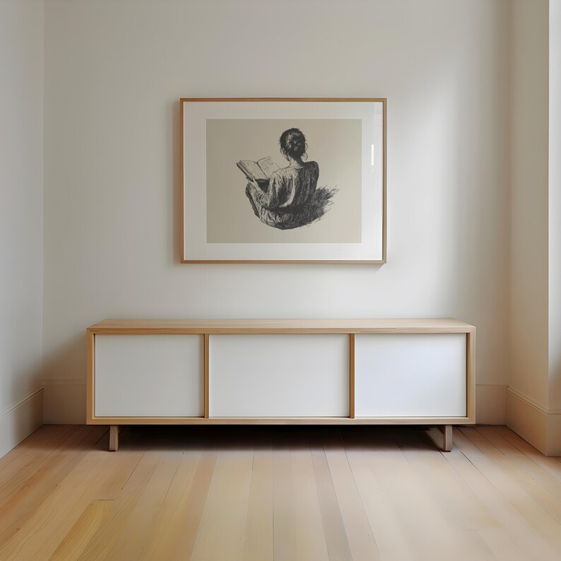Pu&ograve; includere: Un mobile in legno chiaro con tre ante bianche. Il mobile &egrave; posto su un pavimento in legno chiaro. Un disegno in bianco e nero incorniciato di una persona seduta e che legge un libro &egrave; appeso al muro sopra il mobile.