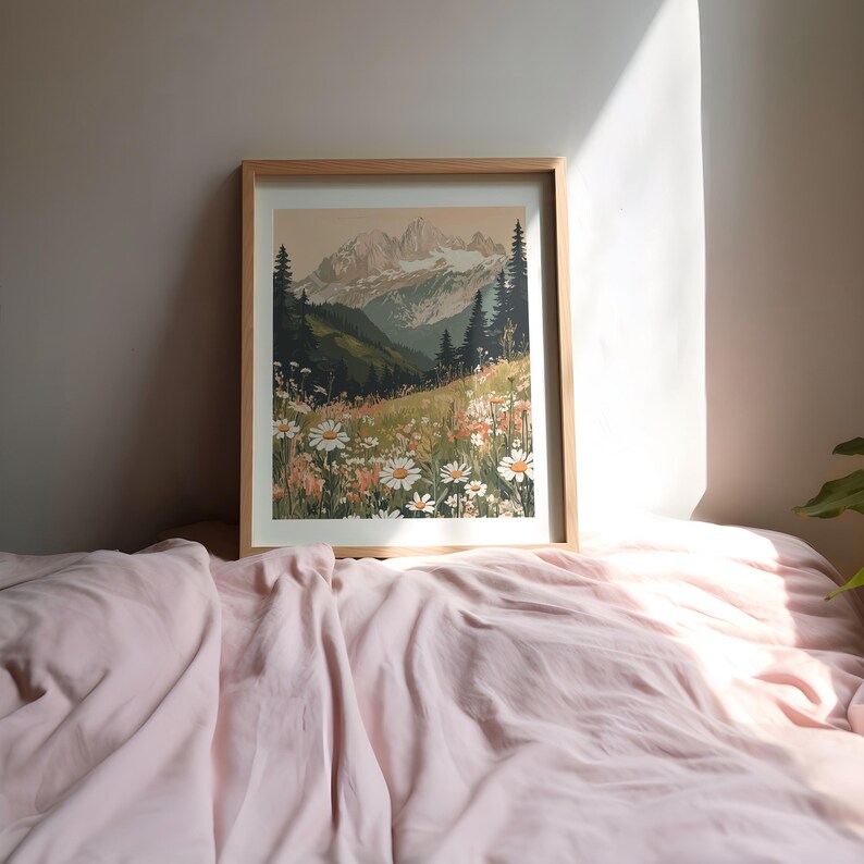 May include: A framed print of a mountain landscape with a field of white daisies in the foreground. The mountains are snow-capped and the sky is a light blue.