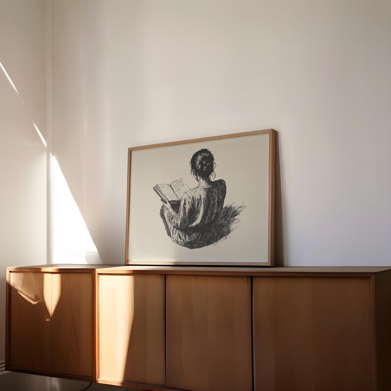 Pu&ograve; includere: Un'illustrazione in bianco e nero di una persona seduta e che legge un libro. L'illustrazione &egrave; incorniciata e appesa a un muro sopra un armadio in legno.