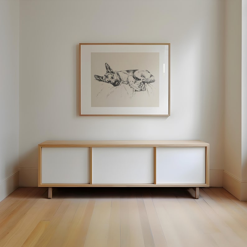 K&ouml;nnte beinhalten: Ein wei&szlig;er Schrank mit drei Schiebet&uuml;ren steht auf einem Holzboden vor einer wei&szlig;en Wand. Ein gerahmtes Schwarzwei&szlig;bild eines Hundes h&auml;ngt an der Wand &uuml;ber dem Schrank.