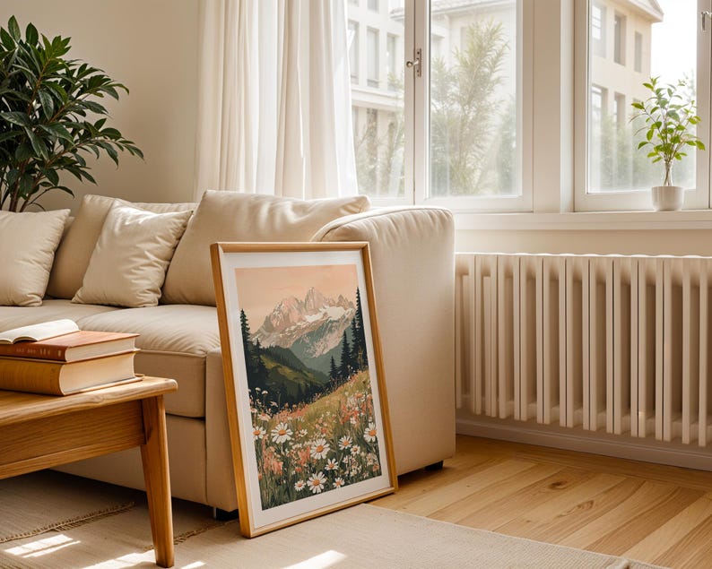 May include: A framed print of a mountain landscape with a field of white flowers in the foreground. The mountains are a soft pink and orange color, and the sky is a light blue. The print is in a wooden frame.