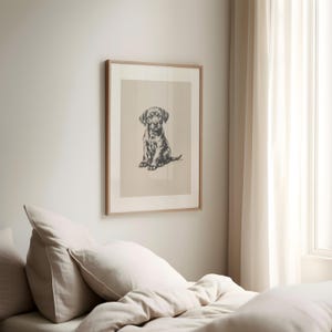 May include: A framed black and white illustration of a Labrador Retriever puppy sitting. The puppy is looking directly at the viewer. The frame is a light wood color.