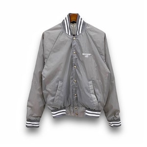 May include: A grey bomber jacket with a button-up front, featuring white and grey striped details on the collar, cuffs, and hem. The jacket has two front pockets and the word "SHARP" printed on the chest.