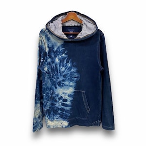 Puede incluir: Una sudadera con capucha azul tie-dye con una franja blanca en la capucha. La sudadera tiene un bolsillo canguro y una cremallera.