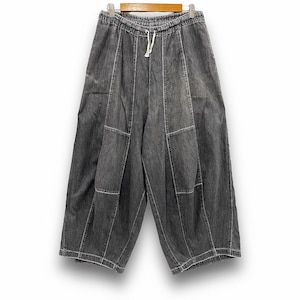 May include: Gray denim culottes with a drawstring waist and white stitching. The wide-leg pants are hanging on a wooden hanger against a white background. The culottes have a relaxed fit and a unique panel design.