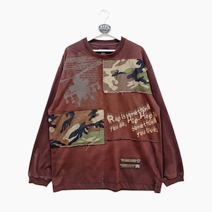 May include: Brown long-sleeved shirt with a patchwork design featuring camouflage fabric and a graphic print that says "Rap is something you do, Hip-Hop is something you live."