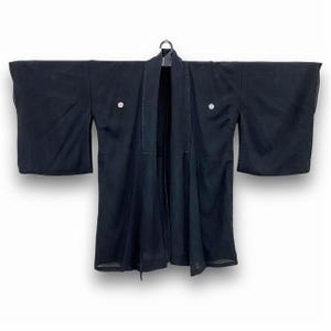Könnte beinhalten: Ein schwarzer Kimono mit zwei dekorativen Knöpfen auf der Vorderseite.