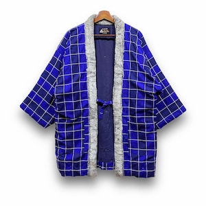 Könnte beinhalten: Blaue Steppjacke mit Gittermuster und weißen Nähten. Die Jacke hat einen grauen Kunstfellbesatz am Kragen und an den vorderen Kanten. Sie hat einen Kordelverschluss und zwei Vordertaschen. Die Jacke hängt an einem Holzbügel.