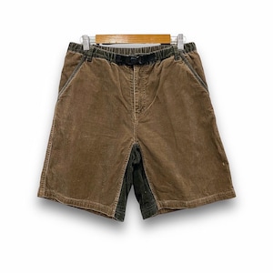 May include: Brown corduroy shorts with a black belt and dark green accents. The shorts are hanging on a wooden hanger. The shorts have pockets and a button closure.