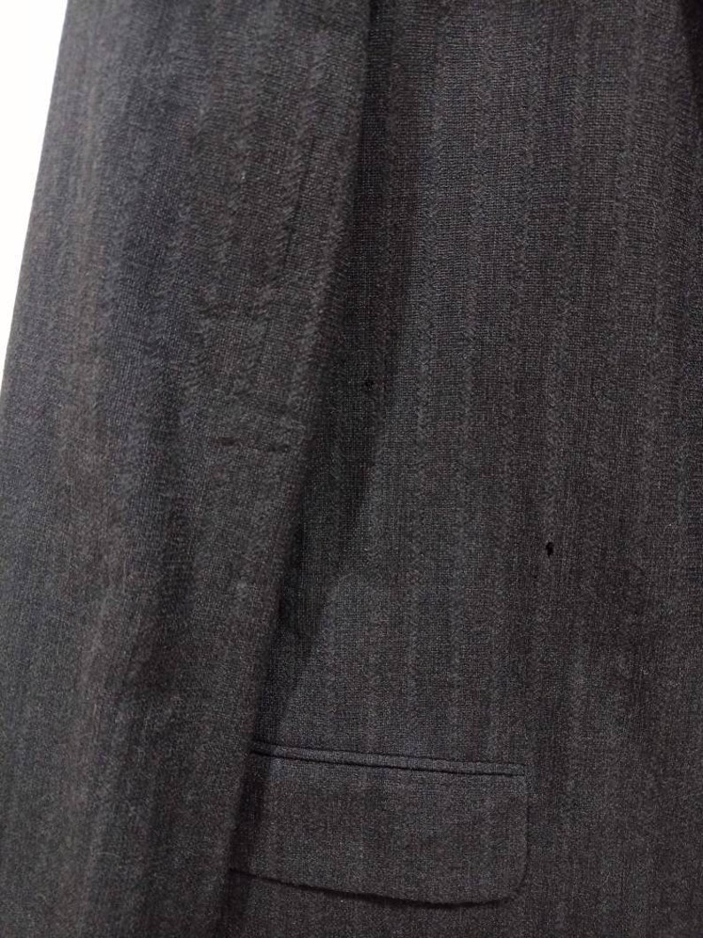 Op de afbeelding: Een donkergrijze blazer met &eacute;&eacute;n zak aan de linkerkant.